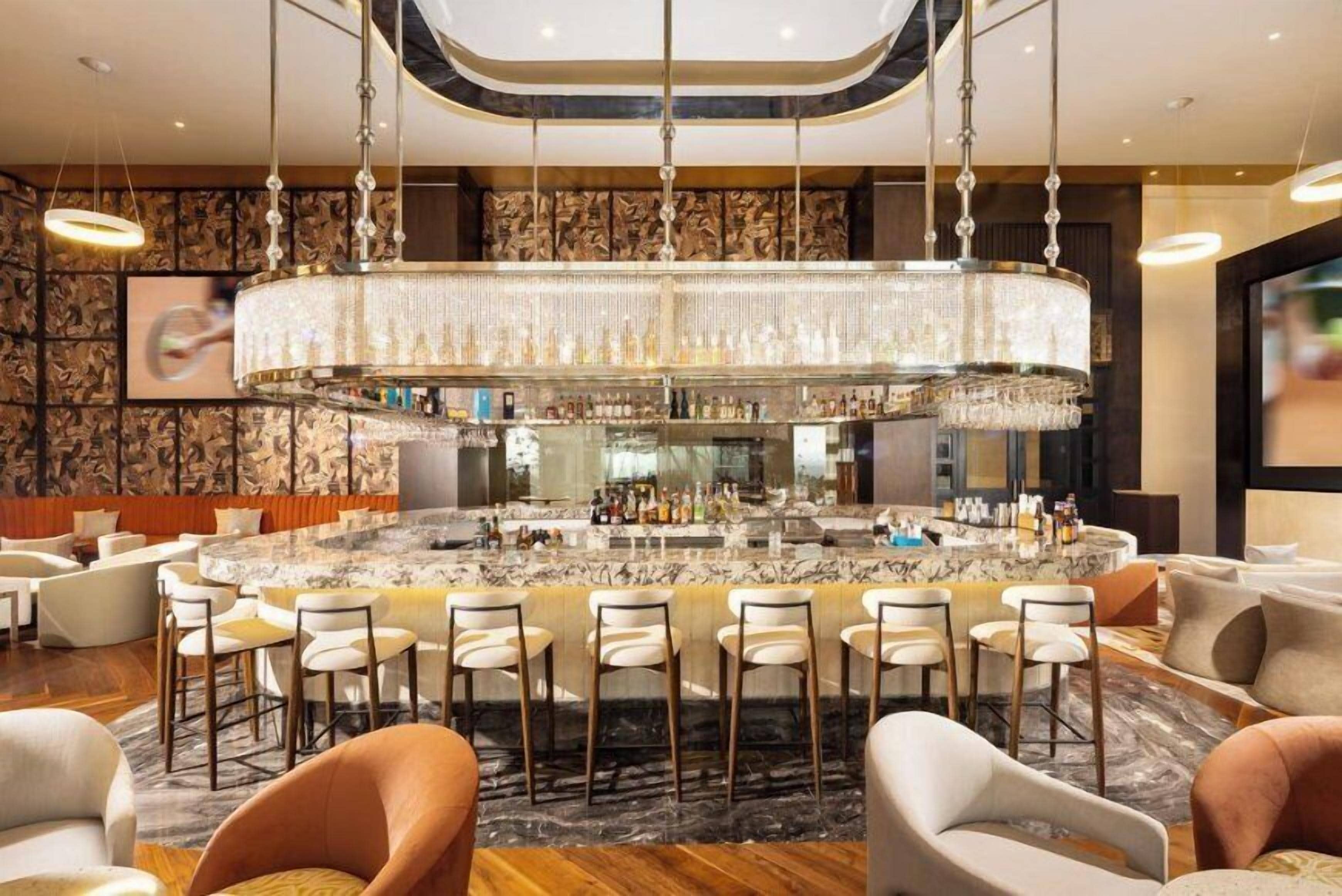 A bar area with a marble countertop, multiple bar stools, and a large chandelier.