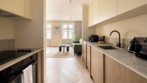 Una cocina moderna con estufa integrada, un lavamanos y una encimera. En el fondo, hay una zona de comedor con una mesa y sillas.