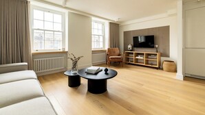 En moderne stue med sofa, sofabord, stol, fjernsyn og radiator.