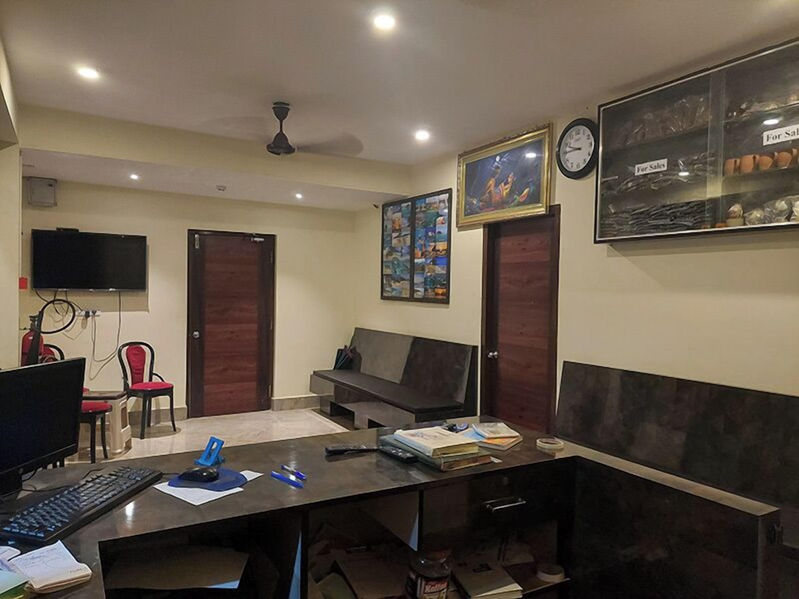 A room with a desk, computer, chair, sofa, and artwork on the walls.