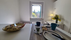 Ruokailutila, jossa on kahdelle katettu pöytä, ikkuna, josta on näkymä, lamppu ja maljakko kukkineen.