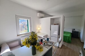 A compact kitchen with a window, a radiator, a refrigerator, and a dining area with a table and chairs.