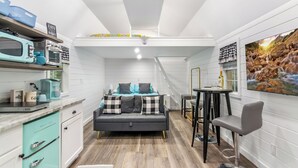 Una cocina compacta con comedor, un sofá y un televisor mostrando un paisaje montañoso.