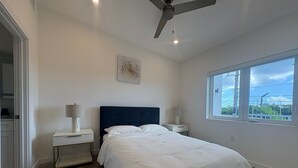 Een slaapkamer met een groot bed, twee nachtkastjes met lampen, een plafondventilator en een raam met uitzicht op groen.