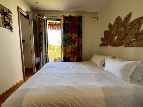A bedroom with a bed, white pillows, a door leading to a balcony, and a wall with a leaf pattern. - Faré de La Vahiné 3 Pièces Mandara Beach (Antibes)