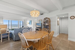 Ein geräumiger Essbereich mit Holztisch und -stühlen, einer Chandelüster und Meerblick durch große Fenster.