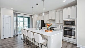 Una cocina moderna con armarios blancos, electrodomésticos de acero inoxidable y una isla central con taburetes de bar.