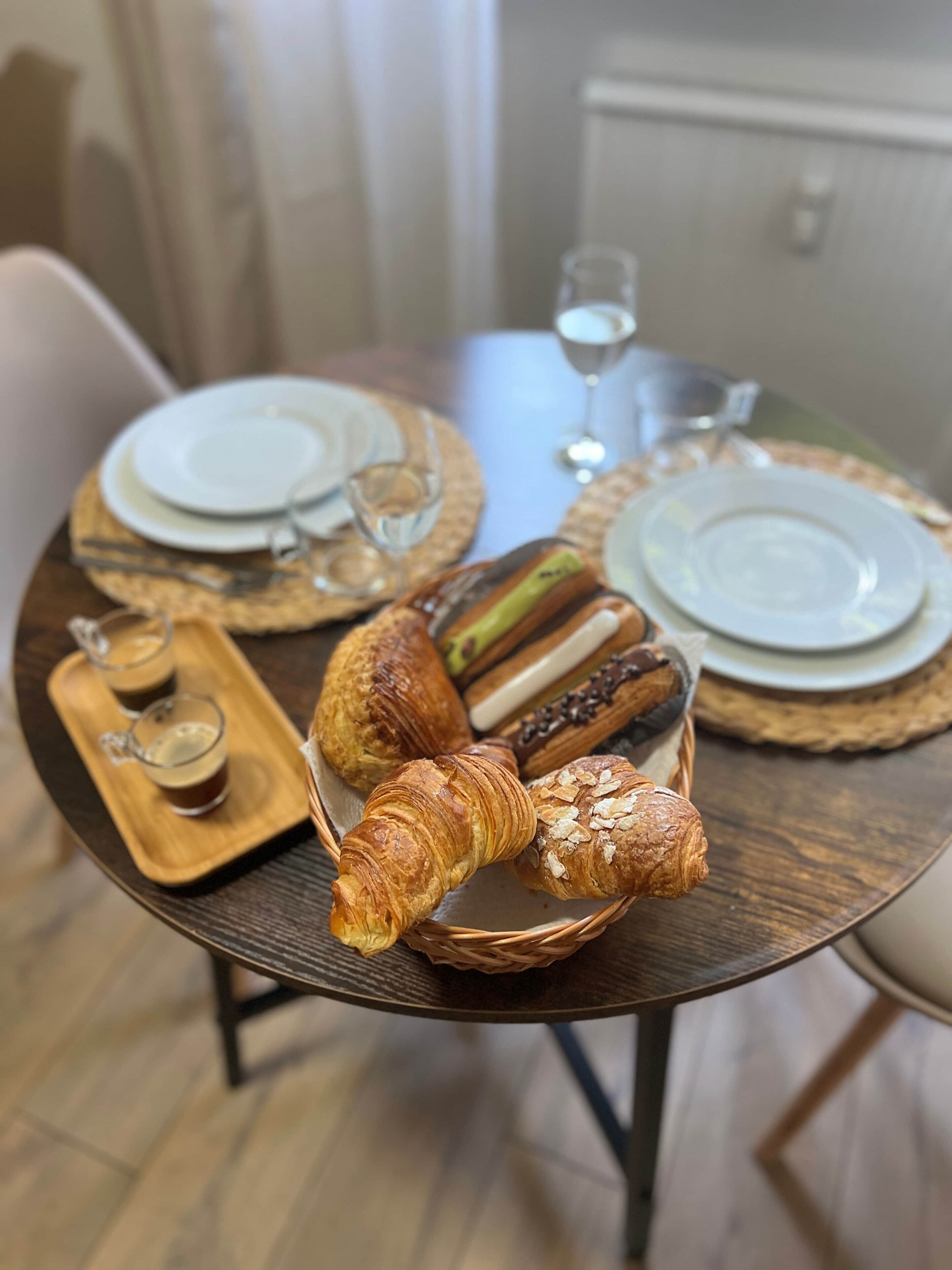 Ruokapöytä, jonka päällä on lautasia, laseja ja kori täynnä leivonnaisia.