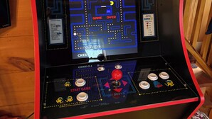 Pac-Man-peliautomaatti, jossa on näyttö, jossa näkyy labyrinttipeli, ohjauspainikkeet ja kolikkopaikka.