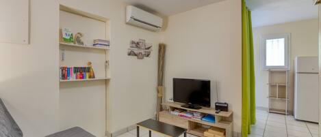 Un espacio habitable compacto con sofá, televisor pequeño, estantería y ventana con cortinas.