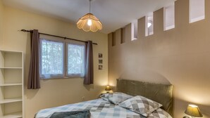 Ein Schlafzimmer mit einem Bett, einem Nachttisch mit Lampe, einem Fenster mit Vorhängen und einer Regaleinheit.