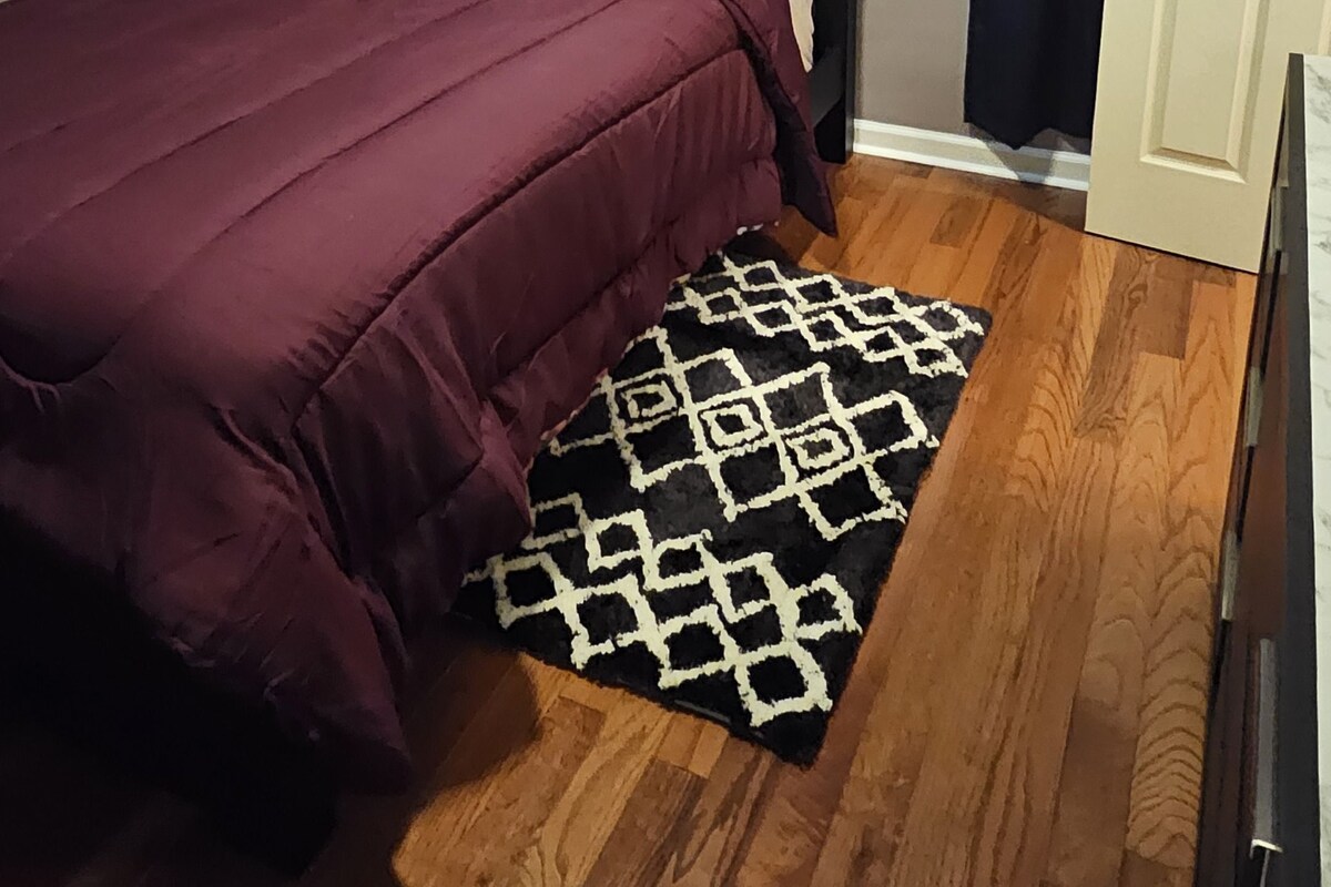 A bedroom with a bed, a patterned rug, a door, and a window with curtains.