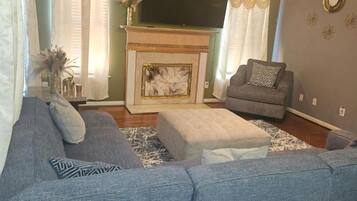 A living room with a fireplace, a sofa, an ottoman, and a television.