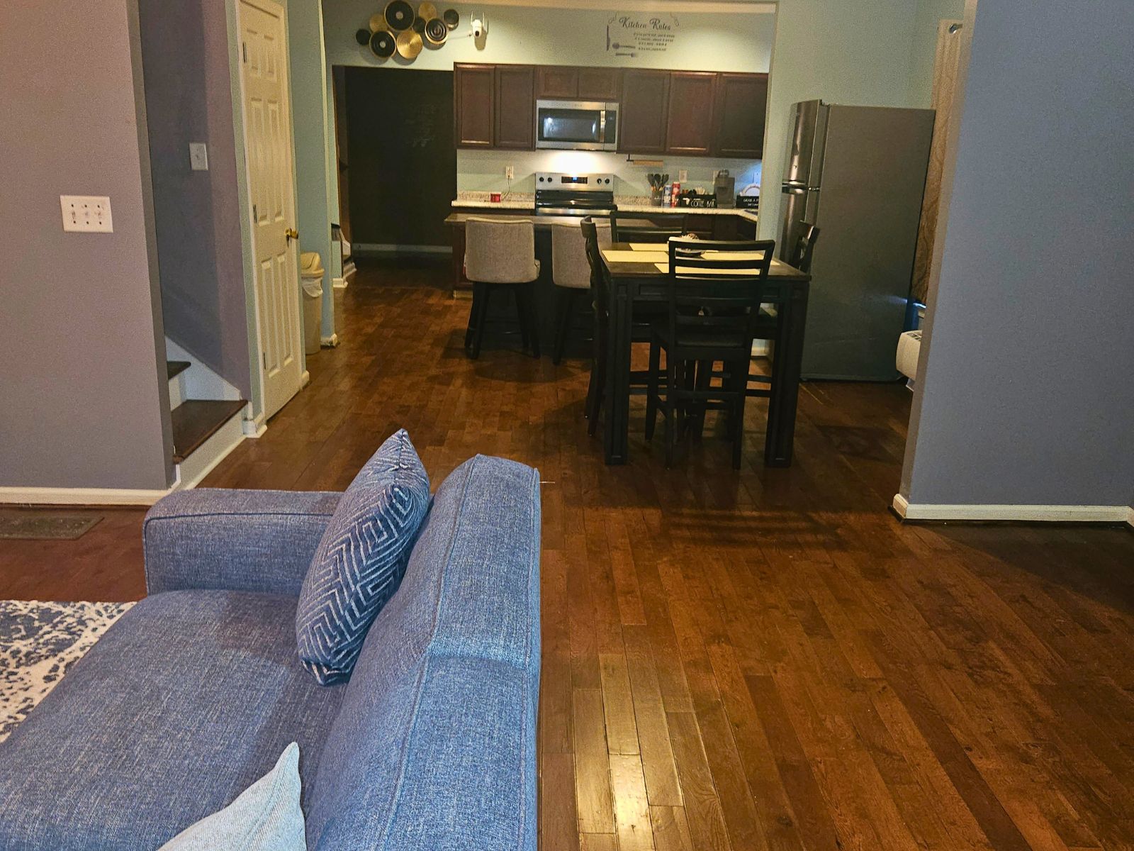 A living room with a sofa, a dining table with chairs, a kitchen area with cabinets and appliances, and a wooden floor.