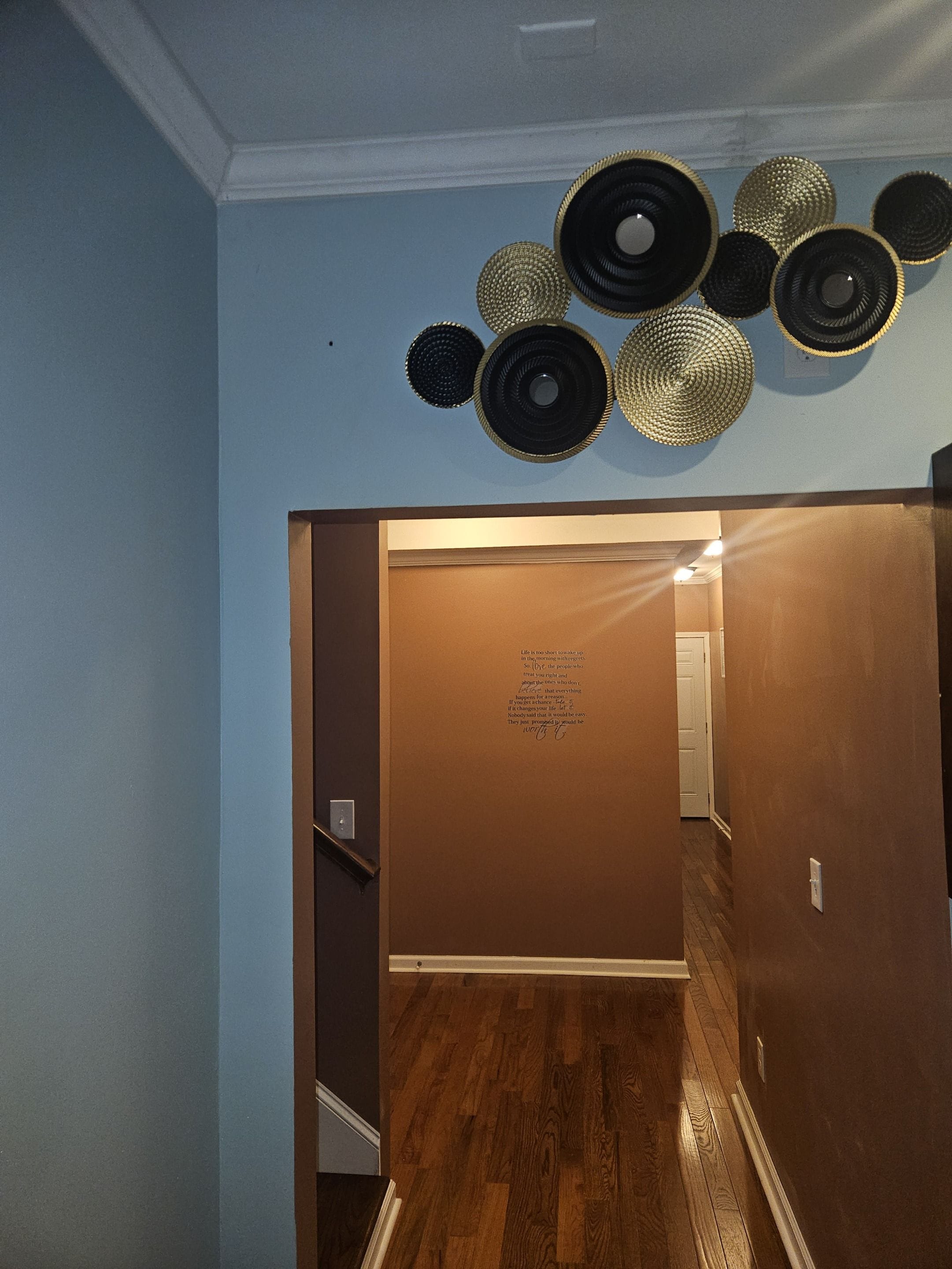 A hallway with a wooden floor, a door with a wall decal, and a ceiling with decorative woven baskets.