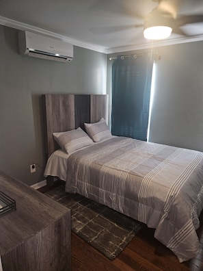 A bedroom with a bed, a ceiling fan, an air conditioning unit, and a window with curtains.