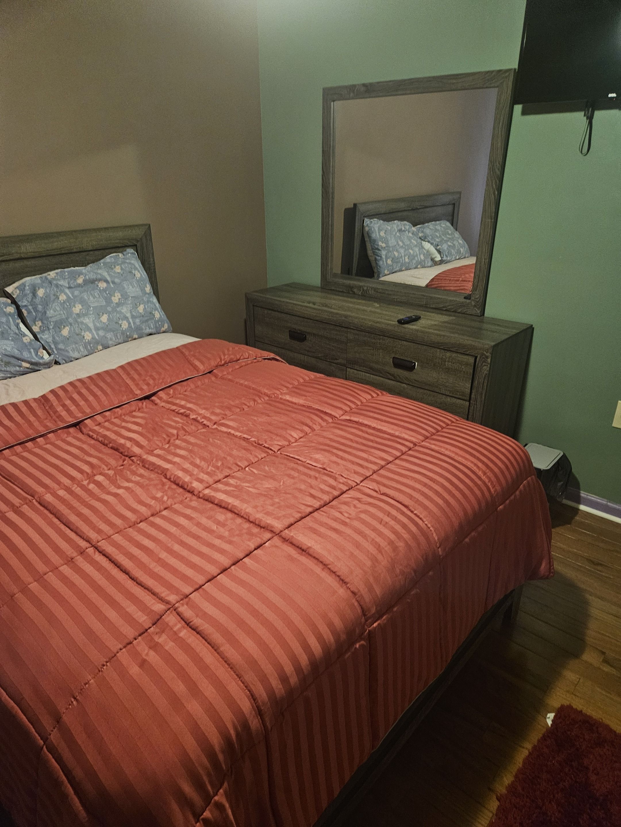A bedroom with a bed, a dresser, a mirror, and a television.