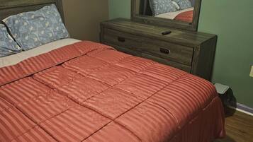A bedroom with a bed, a dresser, a mirror, and a television.