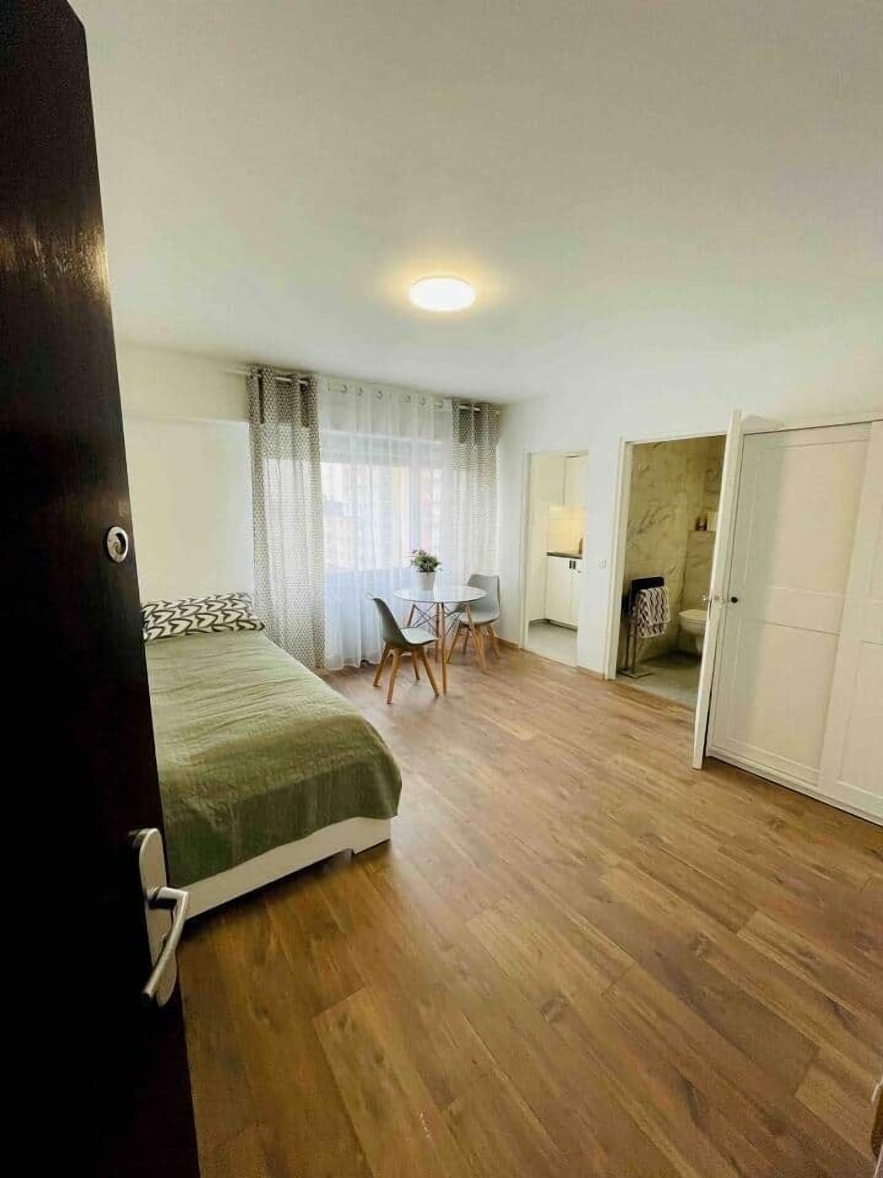 A room with a bed, a desk, and a chair. There is a door leading to another room.