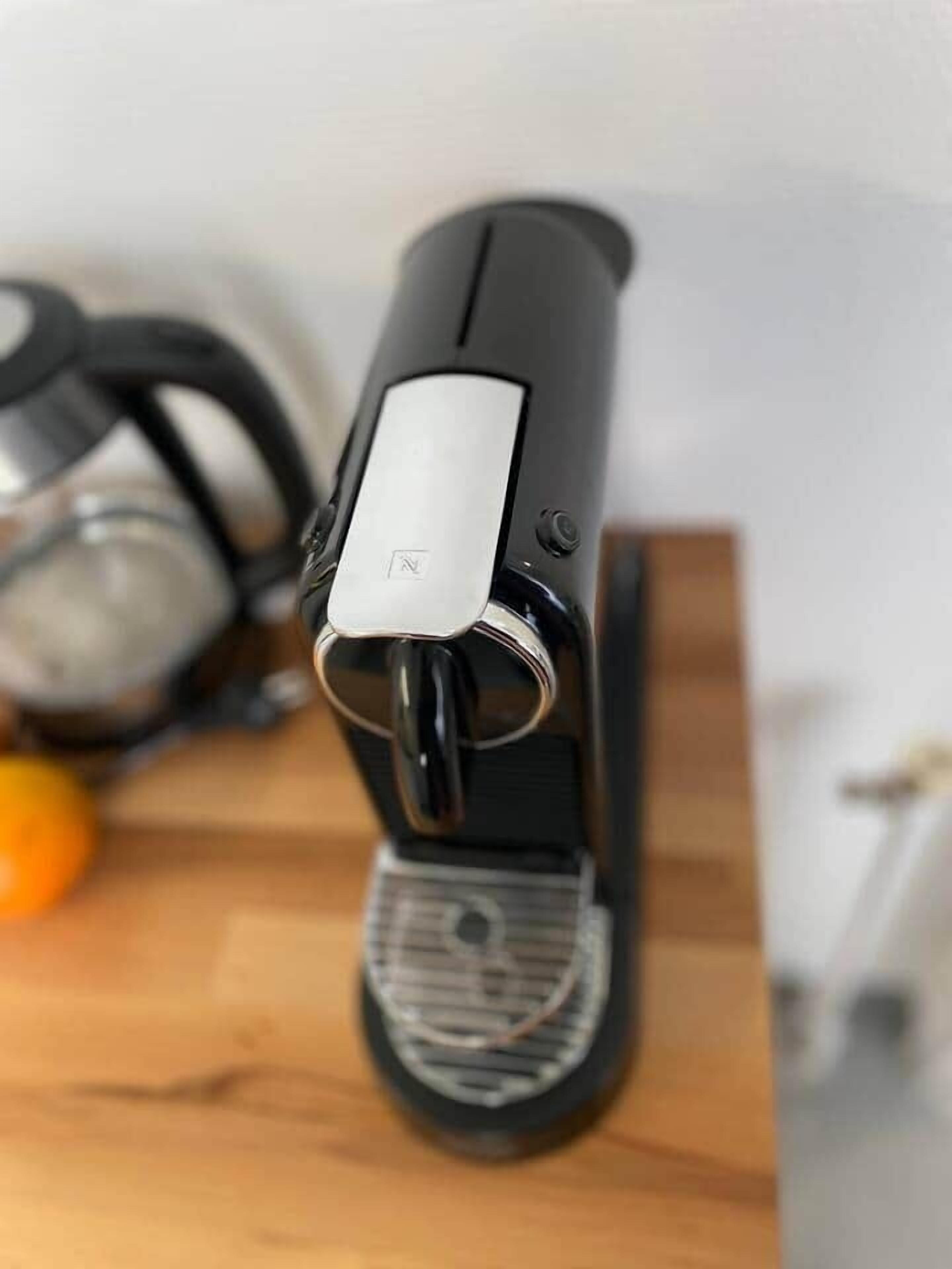 Une machine à expresso noire, avec un bouton argenté sur le dessus, posée sur une surface en bois.