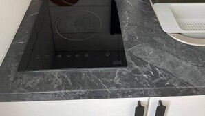 A kitchen with a black induction cooktop, a cork mat, a paper towel holder, and a sink.