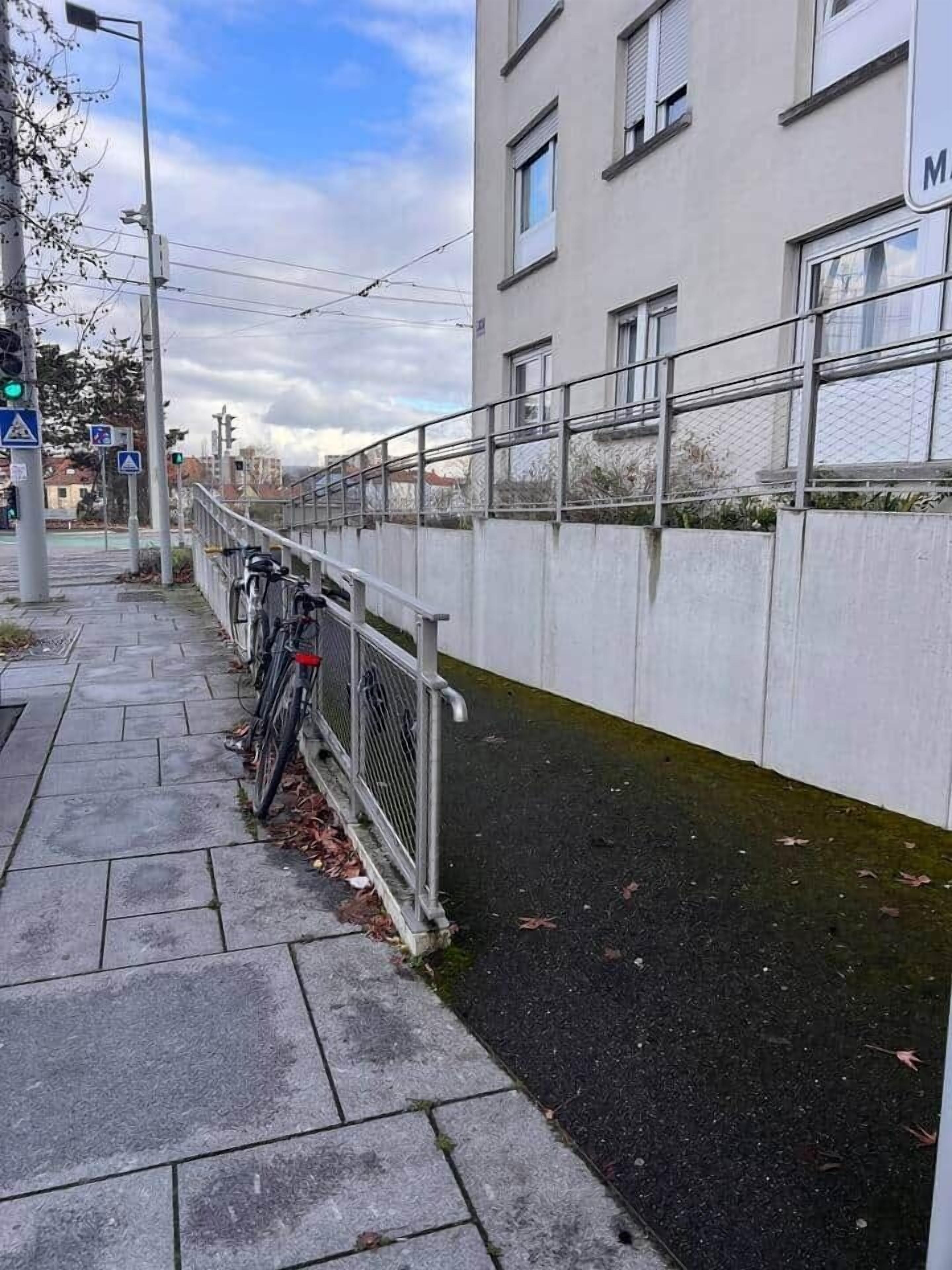 A narrow pathway with a metal railing, a bicycle, and a building with windows.