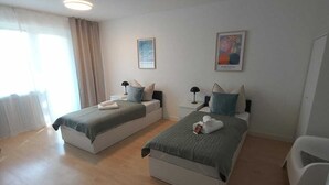 A modern hotel room with two single beds, a small white chair, and a large window with curtains. - Dora - Bergheim near Cologne (Bergheim)