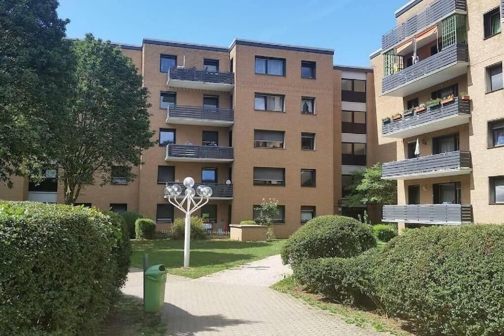 A multi-story residential building with balconies, a central courtyard, and a green space with hedges.