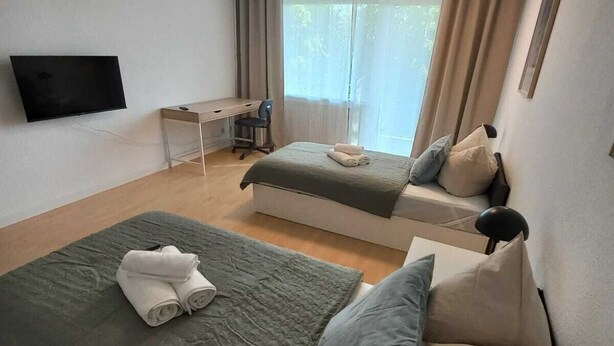 A modern bedroom with two beds, a desk, a chair, a TV, and a window with curtains. - Dora - Bergheim near Cologne (Bergheim)