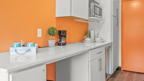 Eine Küche mit weißen Schränken, einer orangefarbenen Wand, einer Mikrowelle, einer Kaffeemaschine und einem Blumentopf.