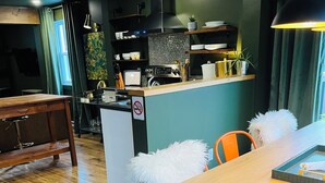 Un comedor moderno con una mesa de madera y sillas anaranjadas, una zona de cocina con cafetera y un cartel de prohibido fumar.