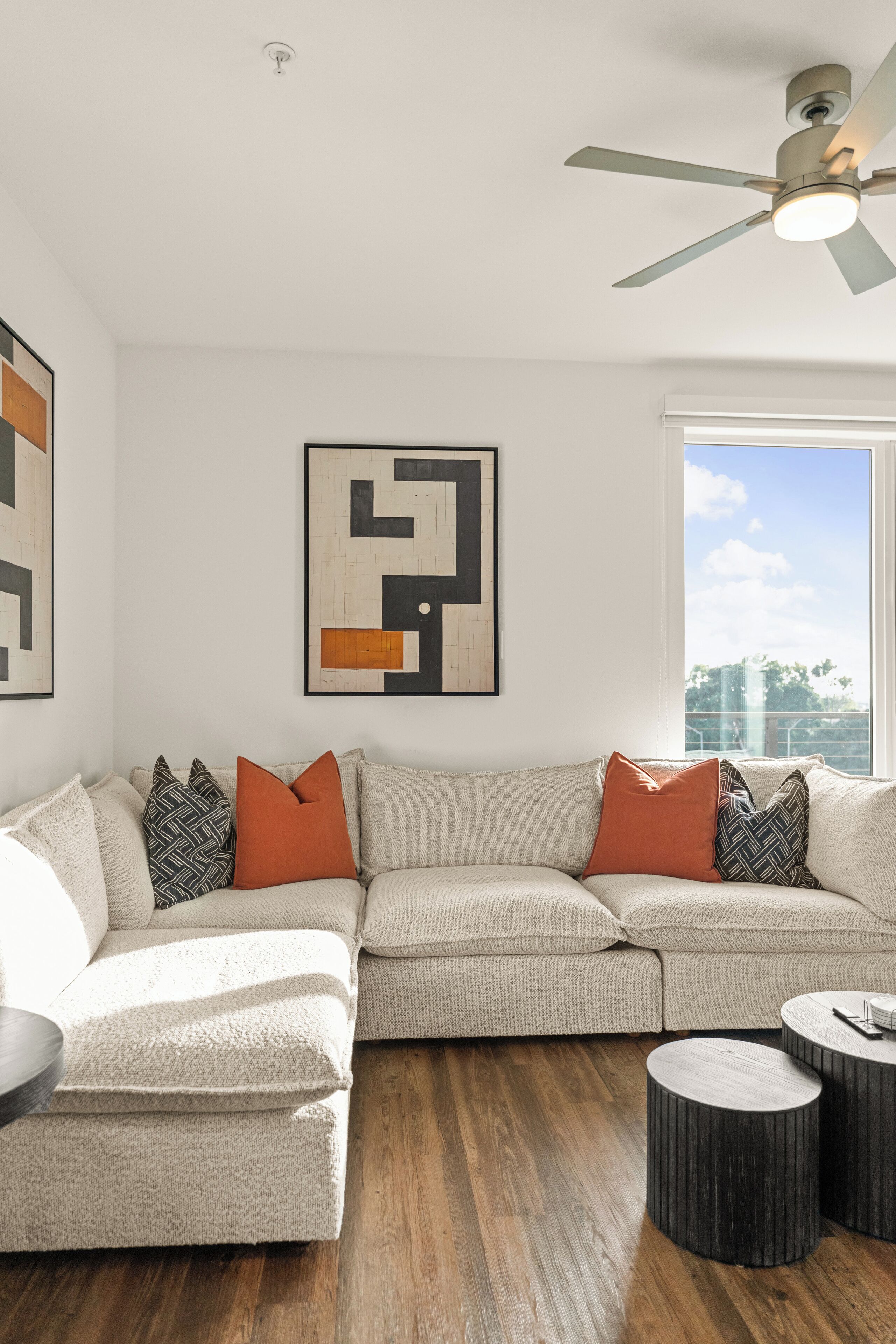 Un salon moderne avec un canapé d’angle, deux petites tables rondes et un ventilateur de plafond.