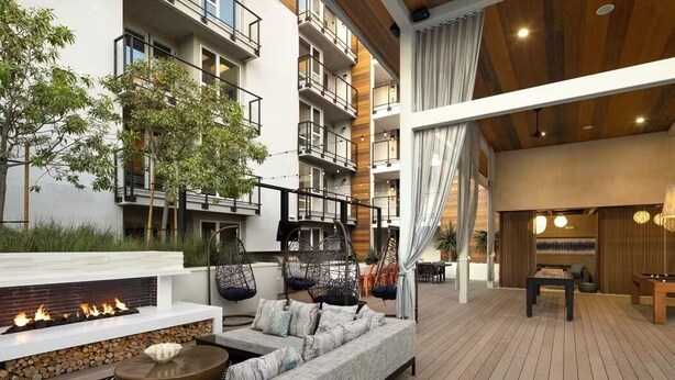 Ett modernt utomhusområde med loungekänsla, komplett med en eldstad, sittplatser och utsikt över byggnadens interiör.