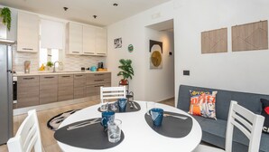 Een moderne keuken met houten kastjes, een eettafel met stoelen en een grijze bank met kussen.