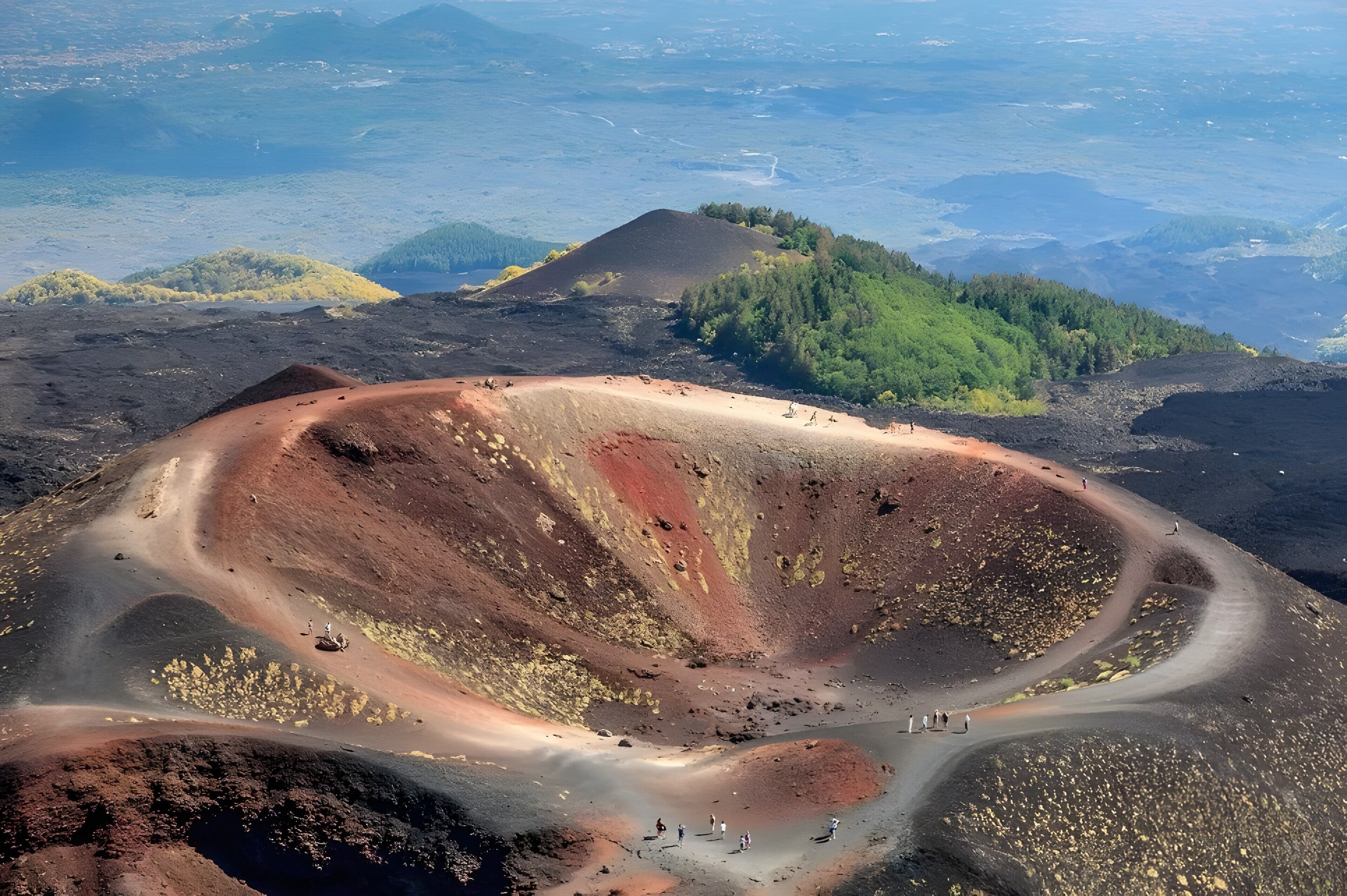 Vue aérienne d’un cratère volcanique, avec une route sinueuse et une végétation clairsemée.