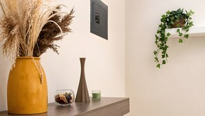 Een houten receptiebalie met een gele vaas, een glazen schaal, een kaars en een lichtschakelaar op de muur.
