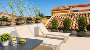 Een terras op het dak met een tafel, stoelen, plantenpotten en een pannendak.