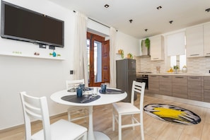 A modern kitchen with a flat-screen TV, white cabinets, and a dining area with a round table and chairs. - MSuite Etna Sicily – Elegant Apartment with Private Terrace between Etna, Taormina & Sea (Macchia)