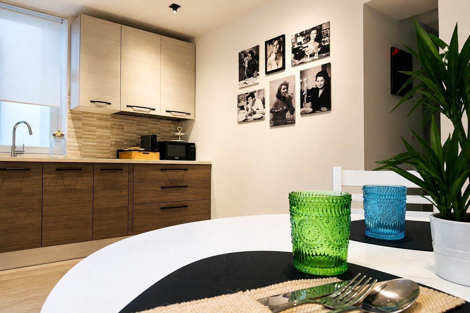 Une cuisine moderne avec des meubles en bois, une table à manger surmontée d’un tapis noir et blanc, et une plante en pot.