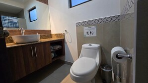 Une salle de bain moderne avec des toilettes blanches, un lavabo avec un receveur et un porte-serviettes. Un panneau avec des instructions est fixé au mur.