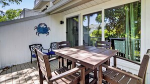 Une terrasse extérieure couverte, avec une table et des chaises en bois, une décoration murale représentant un crabe, et une porte-fenêtre coulissante donnant sur un balcon.