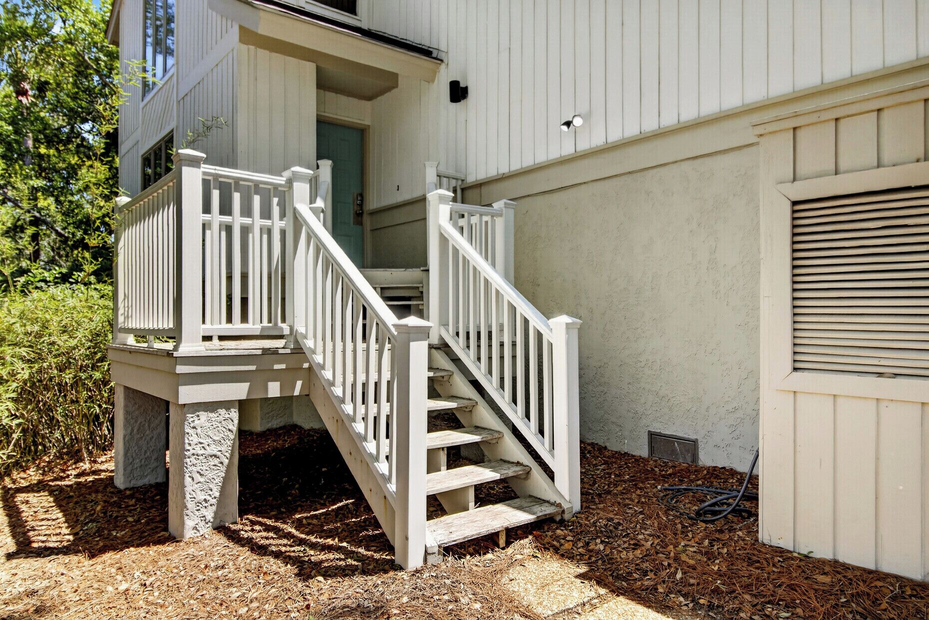 A white wooden staircase leading to a porch with a door, surrounded by mulch and a garden bed.