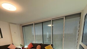 Un salon comprenant un ensemble de canapés, deux petites tables rondes, un tapis et une grande fenêtre avec des stores.