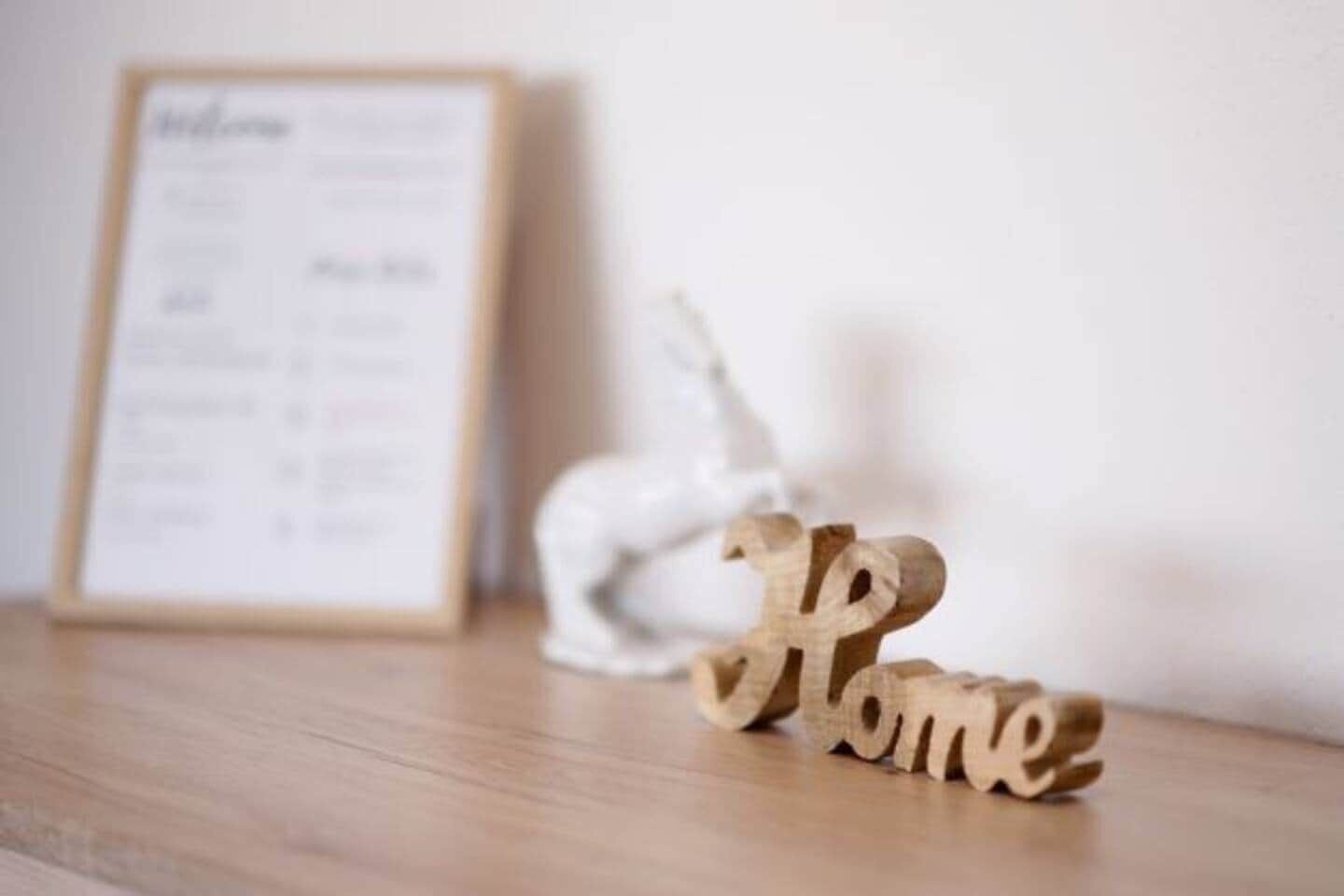 Et træskilt med ordet 'Home' på en træoverflade, en indrammet menu og en hvid genstand i baggrunden.