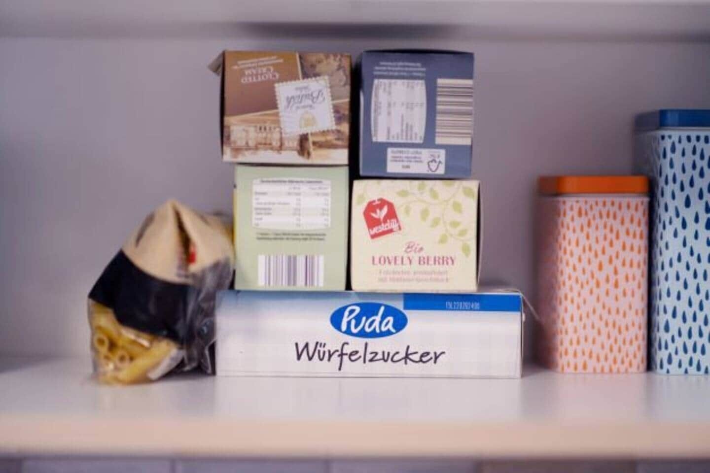 Une étagère contenant diverses boîtes et récipients, dont une boîte étiquetée « Roda Würfelzucker ».