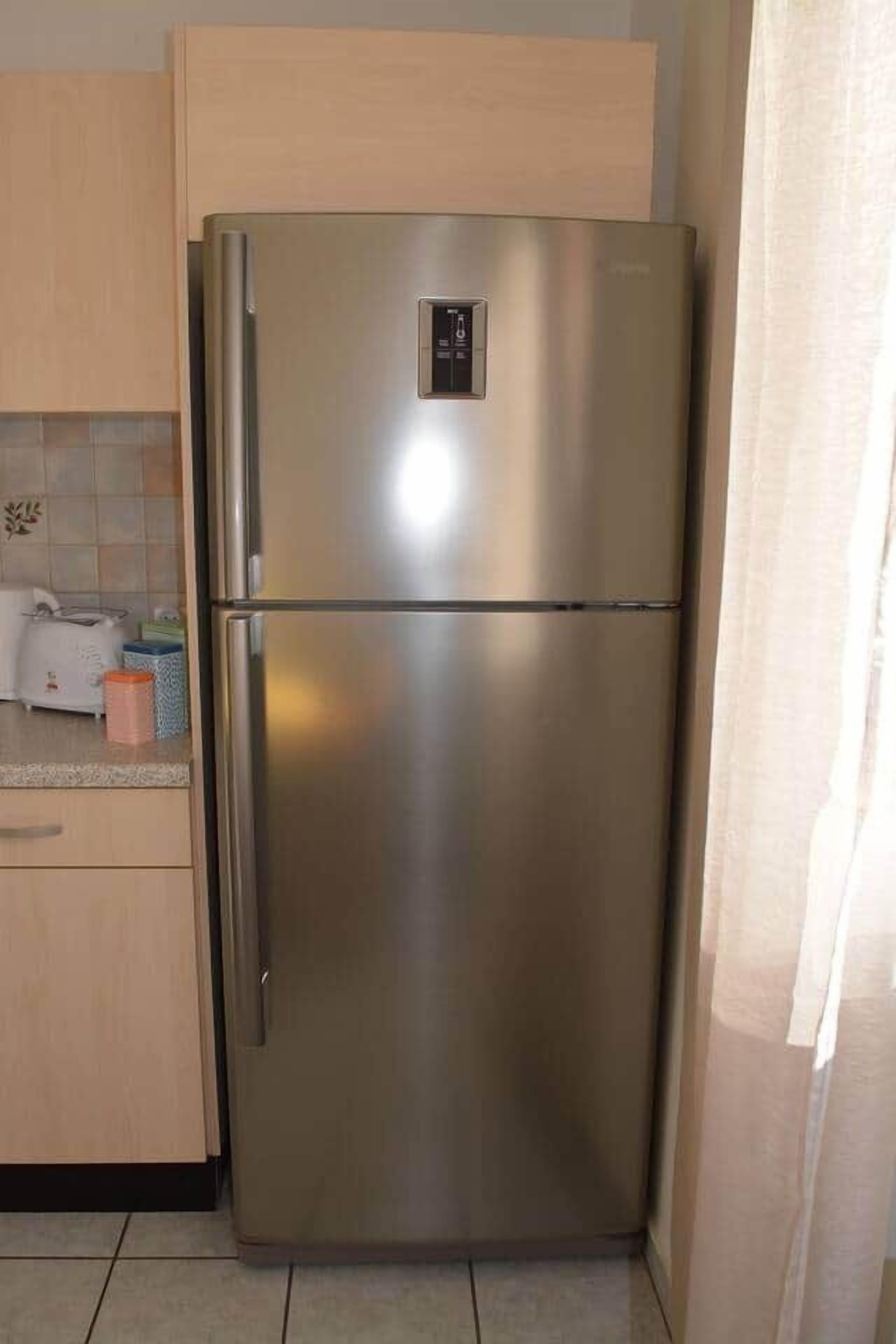 Un refrigerador de acero inoxidable en una cocina con armarios de madera clara y salpicadero de azulejos.