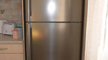 Un refrigerador de acero inoxidable en una cocina con armarios de madera clara y salpicadero de azulejos.