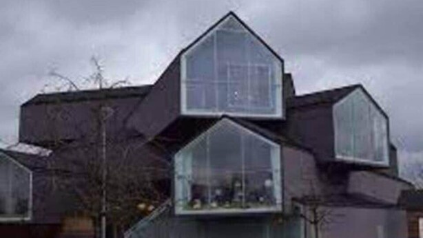 Un bâtiment moderne au design angulaire original, doté de grandes fenêtres en verre et d’une façade sombre.