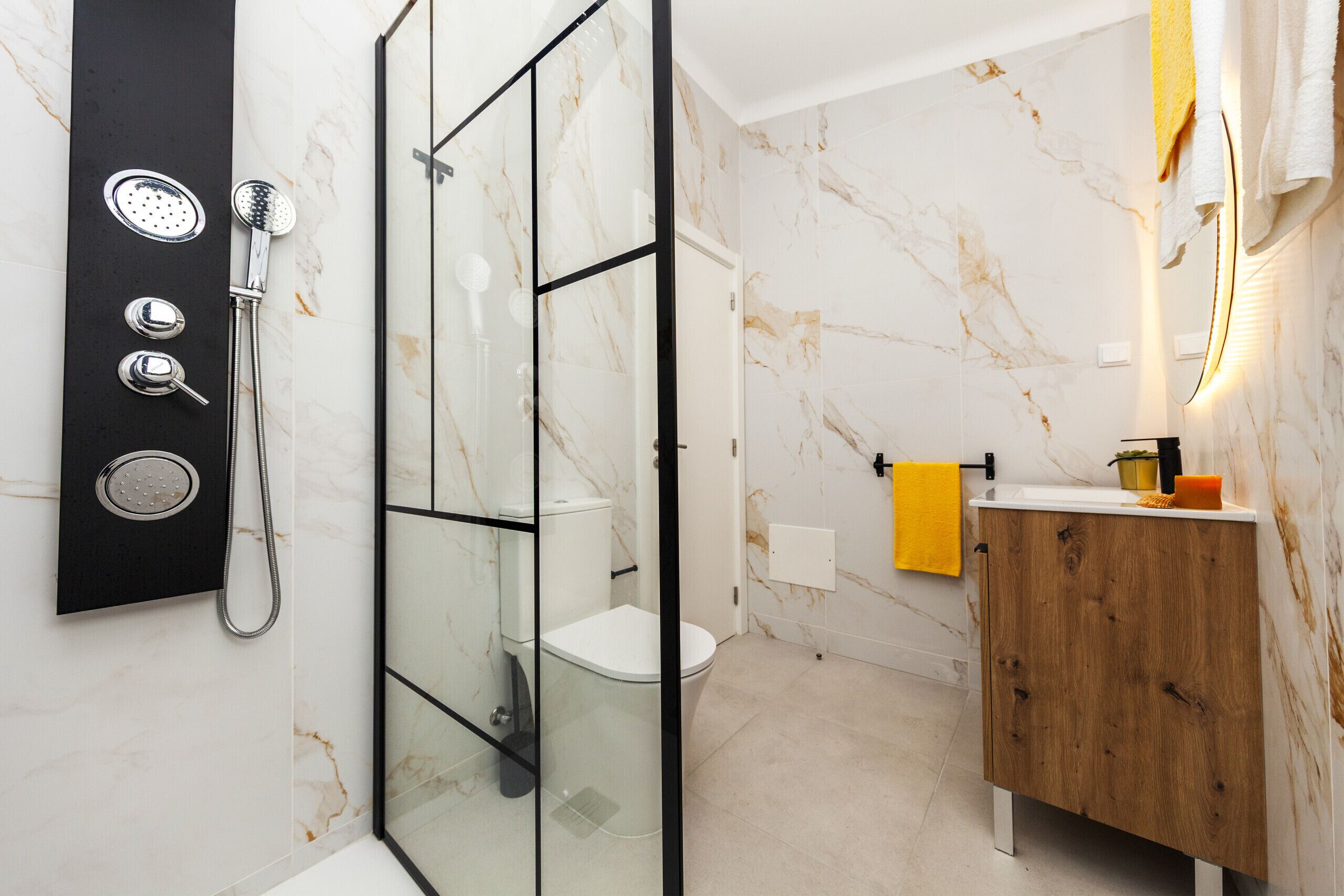 Un baño moderno con ducha de vidrio, inodoro blanco y tocador de madera con espejo.