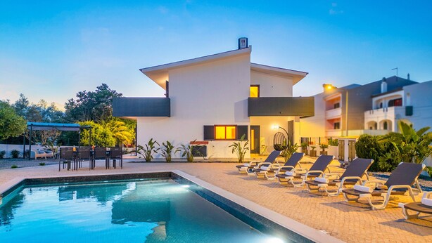 Ein modernes Hotel mit Swimmingpool, Liegestühlen und einer überdachten Außenbereich-Sitzgruppe.